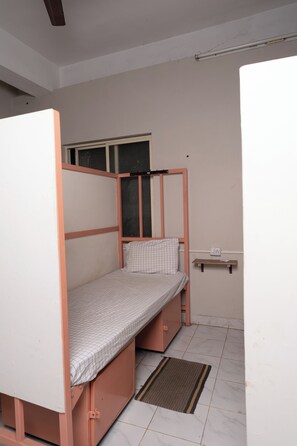 A small, single-bed room with a wooden frame, a window, a bedside table, and a power outlet. - Deep Woods Stay (Kinathukadavu)