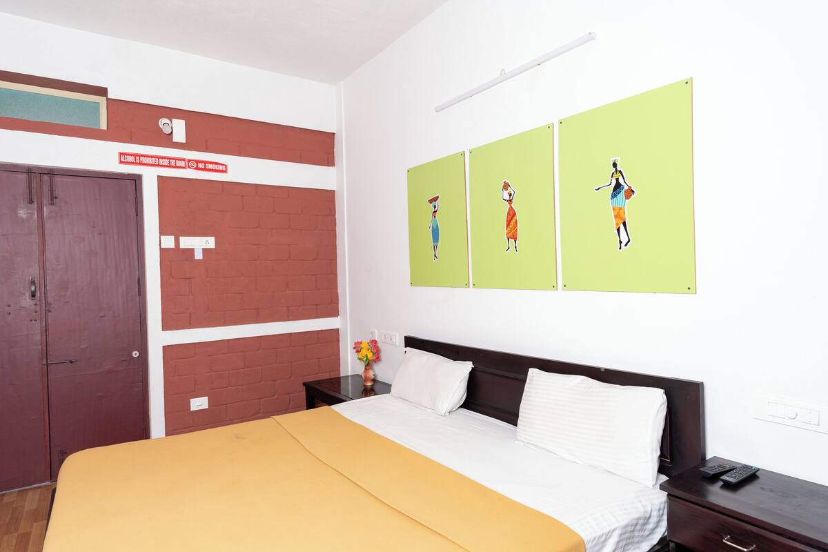 A hotel room with a bed, a nightstand, a wall-mounted artwork, a brick accent wall, and a door with a sign.