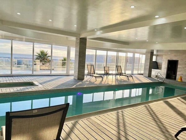 A spacious indoor swimming pool with clear views of the ocean, surrounded by large windows and modern seating. - Rosarito Jr Penthouse at La Jolla Excellence (Playas de Rosarito)