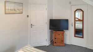 A bedroom with a bed, a television on a wooden cabinet, a door, and a painting on the wall.