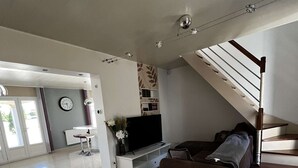 Un salón espacioso con una televisión grande, un sofá marrón y una escalera que sube a un nivel superior.