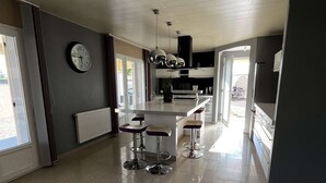Una cocina amplia con una isla central, taburetes de bar, un reloj y un radiador.