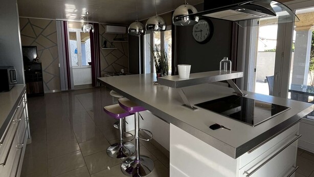 Una cocina moderna con una isla central, electrodomésticos de acero inoxidable, iluminación colgante y vistas al exterior.