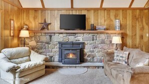 A cozy living room with a stone fireplace, a flat-screen TV mounted above it, and two plush sofas.