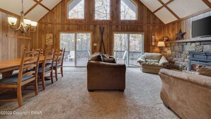 A spacious living room with a high ceiling, wooden beams, a fireplace, and a large TV.
