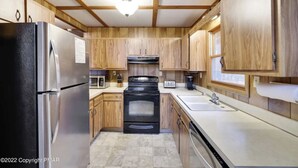 A compact kitchen with wooden cabinets, a stainless steel refrigerator, a black stove, and a sink.