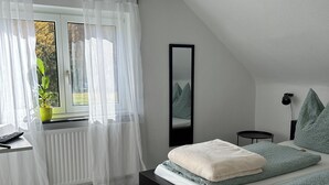 Ein Schlafzimmer mit einem großen Bett, einem Nachttisch, einem Spiegel und einem Fenster mit transparenten Vorhängen.
