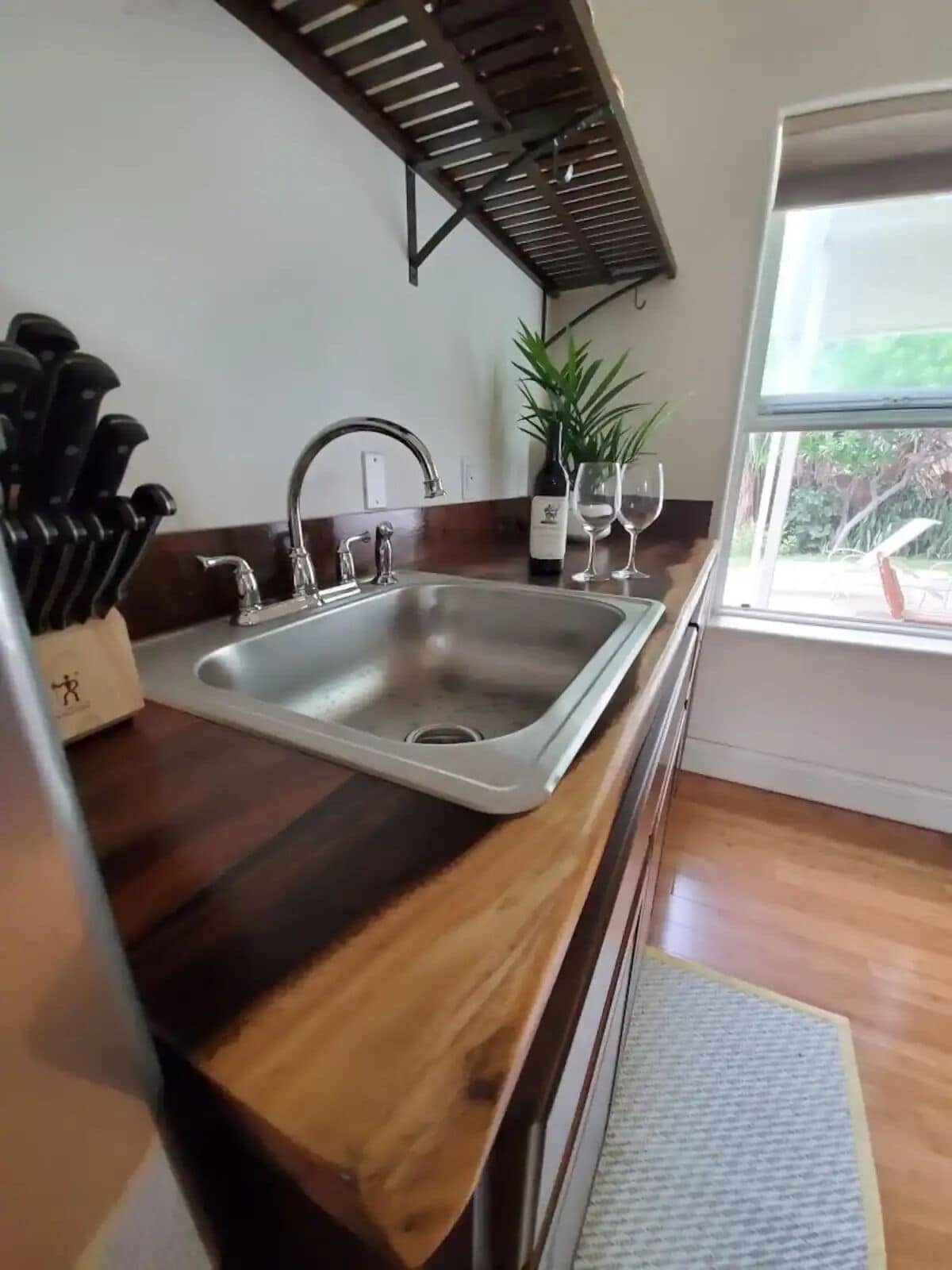 A kitchen with a wooden countertop, stainless steel sink, and a window with a view of greenery.