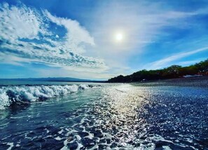 Une plage avec des vagues, un ciel dégagé et des montagnes à l’horizon.