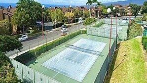 Una cancha de tenis rodeada de una valla, con una carretera y casas al fondo.