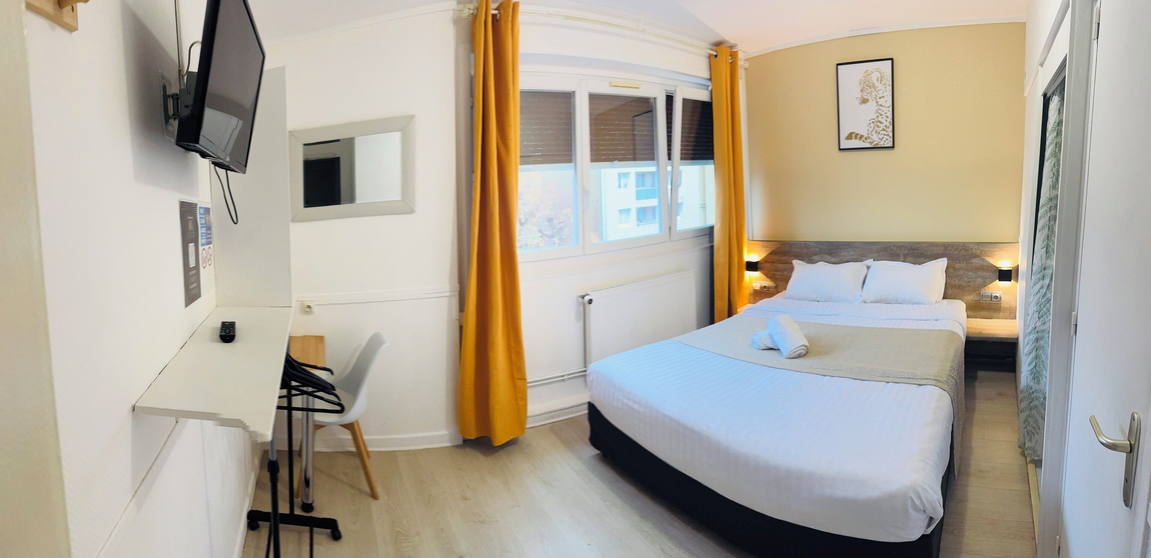 A hotel room with a bed, a desk, a chair, a television, and a window with curtains.