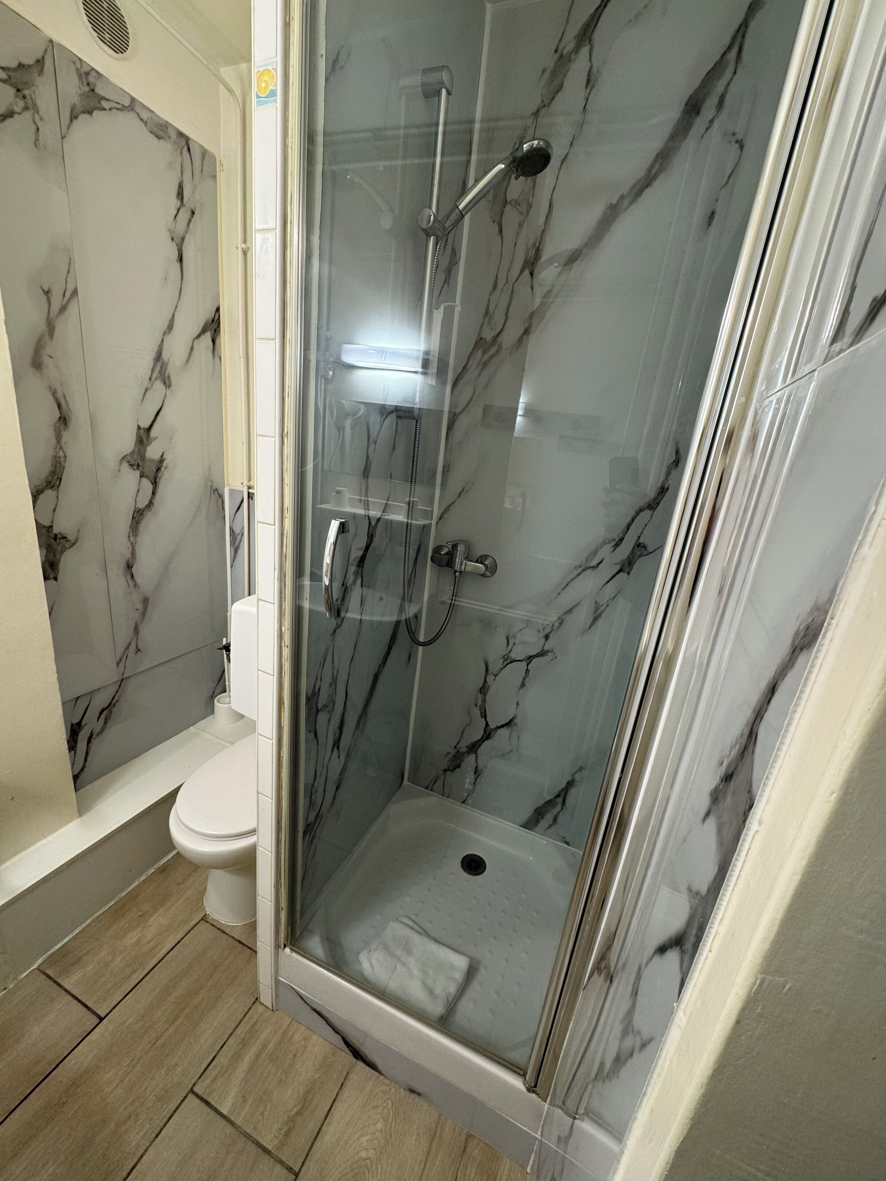 Une cabine de douche fermée par des parois de verre, avec un mur en marbre, des toilettes et un plancher en bois.