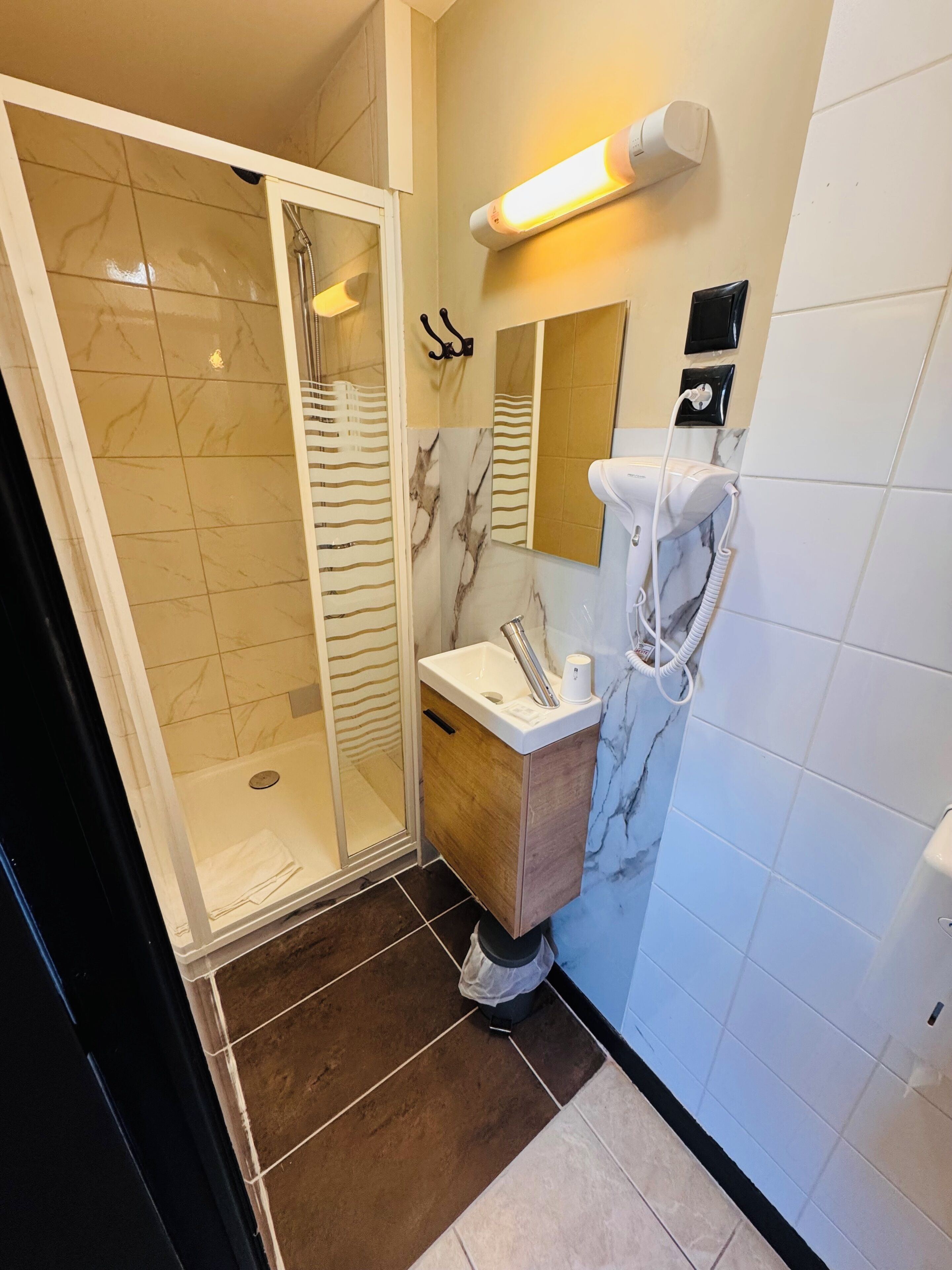 Un baño moderno con ducha envuelta en vidrio, tocador de mármol, secador de pelo integrado y aplique de pared.