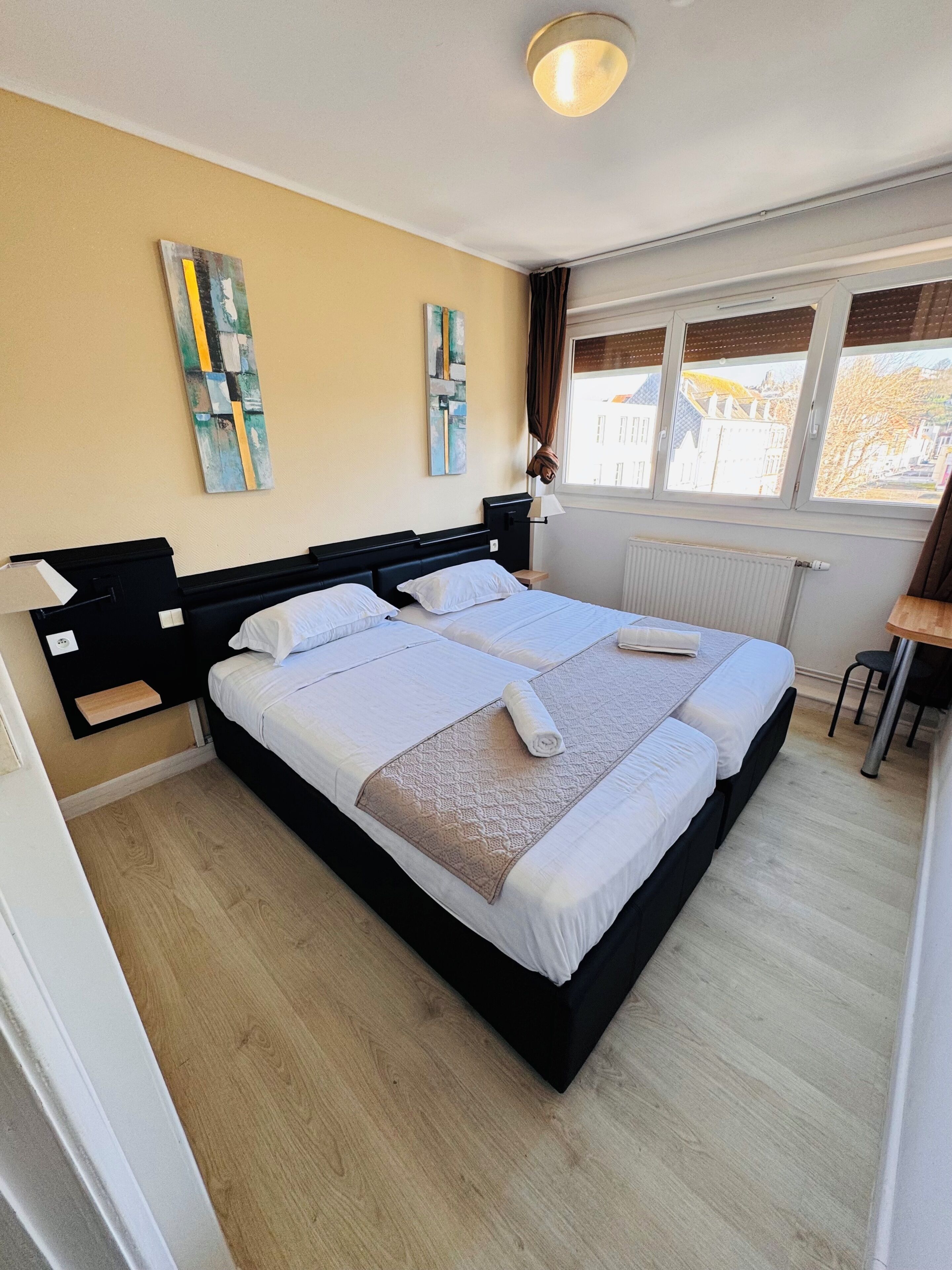 Una cama doble con cabecera, mesitas de noche, un escritorio con silla y una ventana con cortinas.