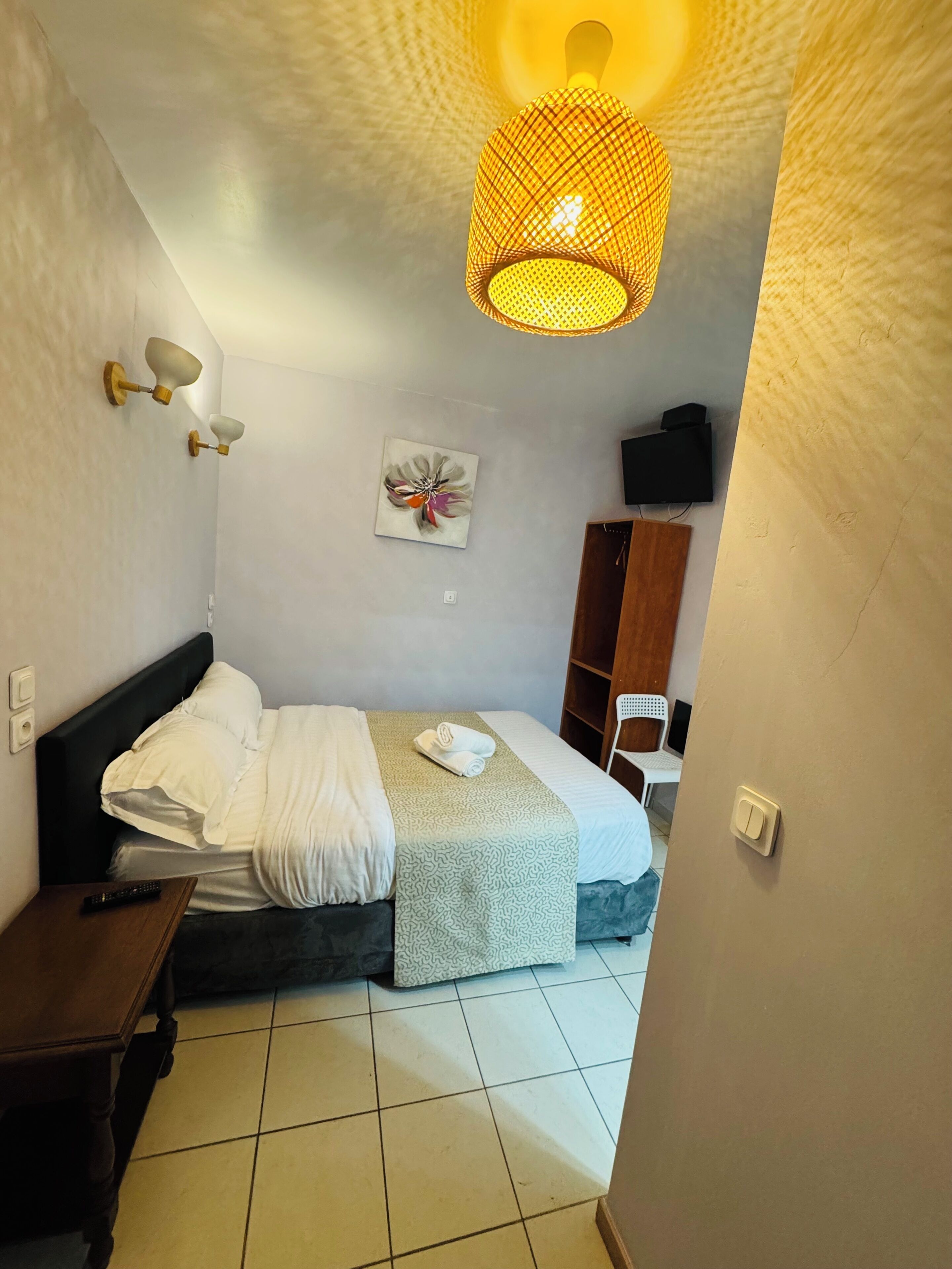 Une chambre d’hôtel comprenant un lit, une table de chevet, une lampe, un tableau décoratif et une armoire.