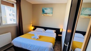 A hotel room with a bed, two bedside tables, a window with curtains, a painting on the wall, and a ceiling light.