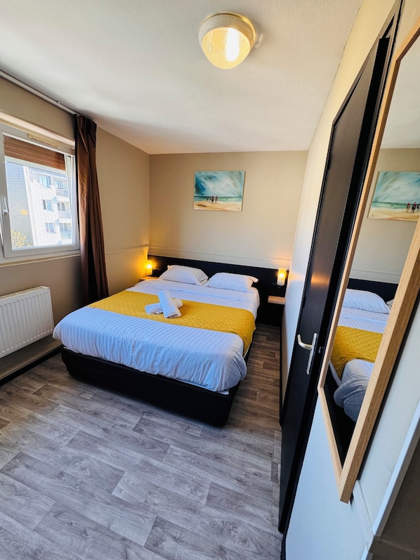 A hotel room with a bed, two bedside tables, a window with curtains, a painting on the wall, and a ceiling light.