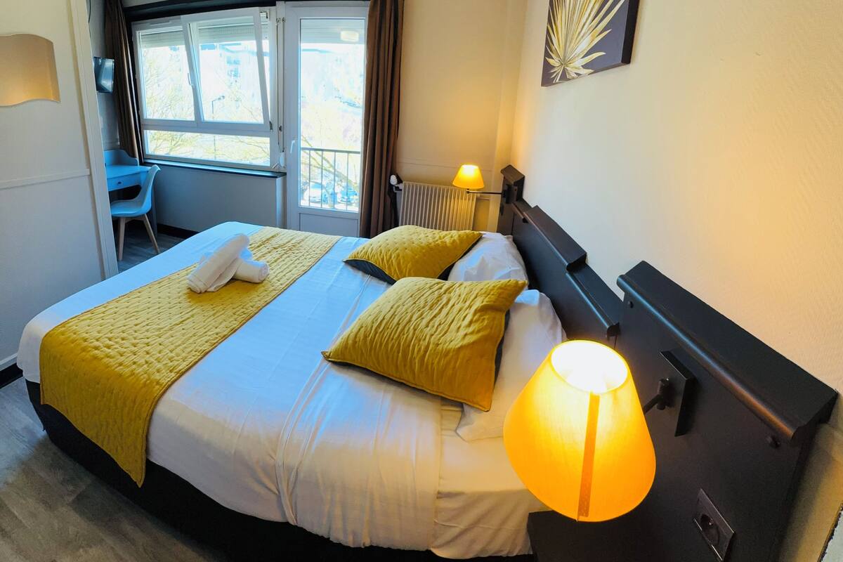 A hotel room with a bed, a desk, a chair, a lamp, and a window with curtains.