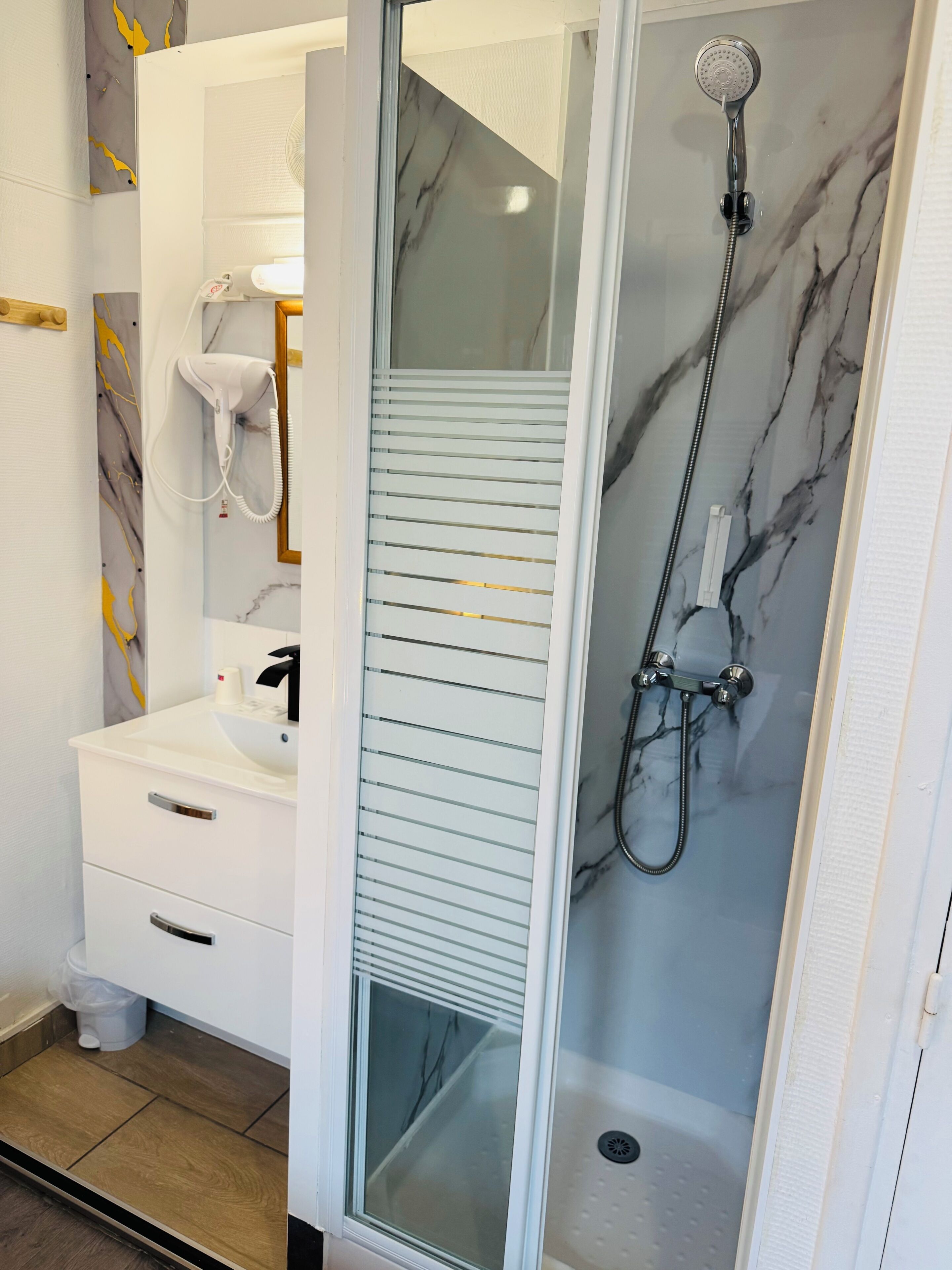 Een badkamer met een witte wastafel, een douchecabine met glazen wanden en een aan de muur bevestigde haardroger.