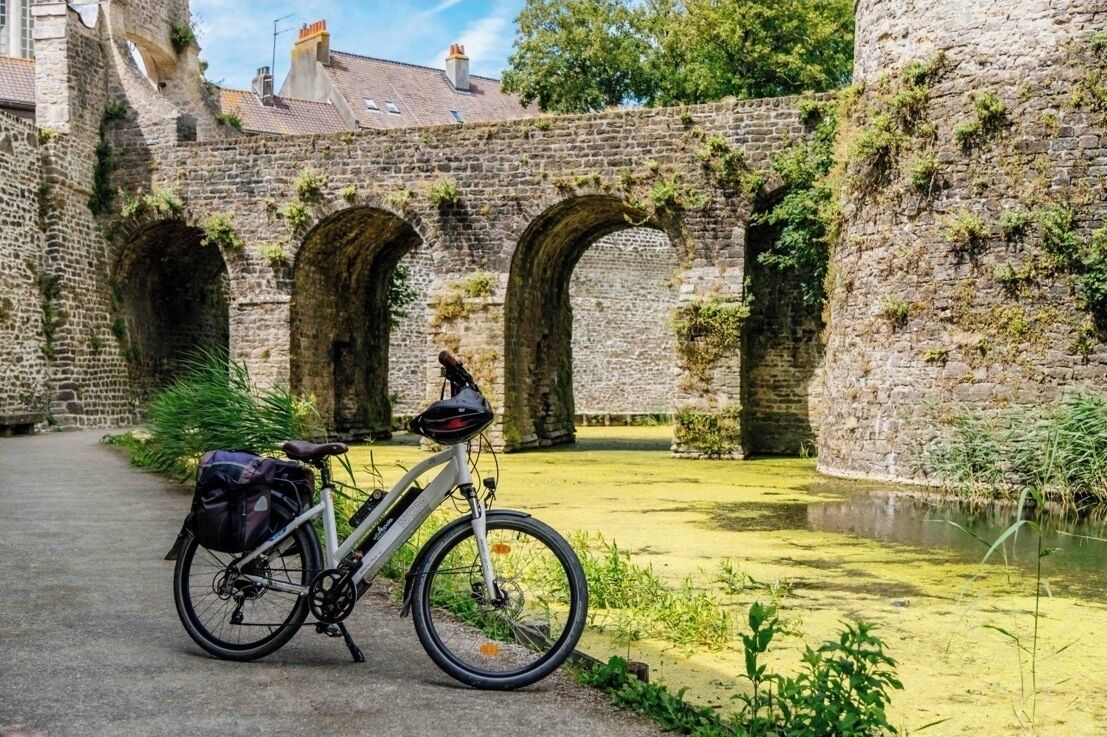 A bicycle parked in front of a historic stone archway with a canal in the background.