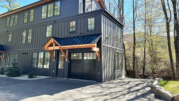 Un bâtiment moderne à deux étages, doté d’une façade sombre, de grandes fenêtres et d’un porche en bois bien visible.