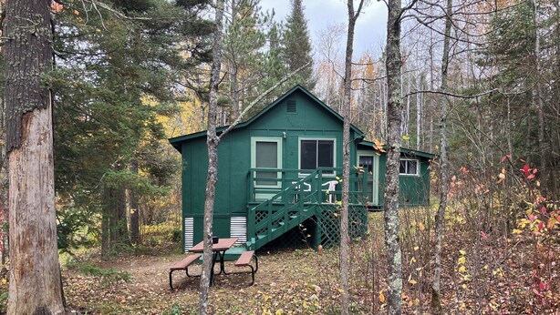 A cabin with a green exterior, a staircase leading to the entrance, and two picnic tables in front. - Cabin 2 "Waterfall" 2 BR, 5-6 pp, access to boats! (Ely)