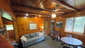 A cozy cabin interior with a wooden ceiling, a gray sofa, a dining table with chairs, and a ceiling fan. - Cabin 2 "Waterfall" 2 BR, 5-6 pp, access to boats! (Ely)