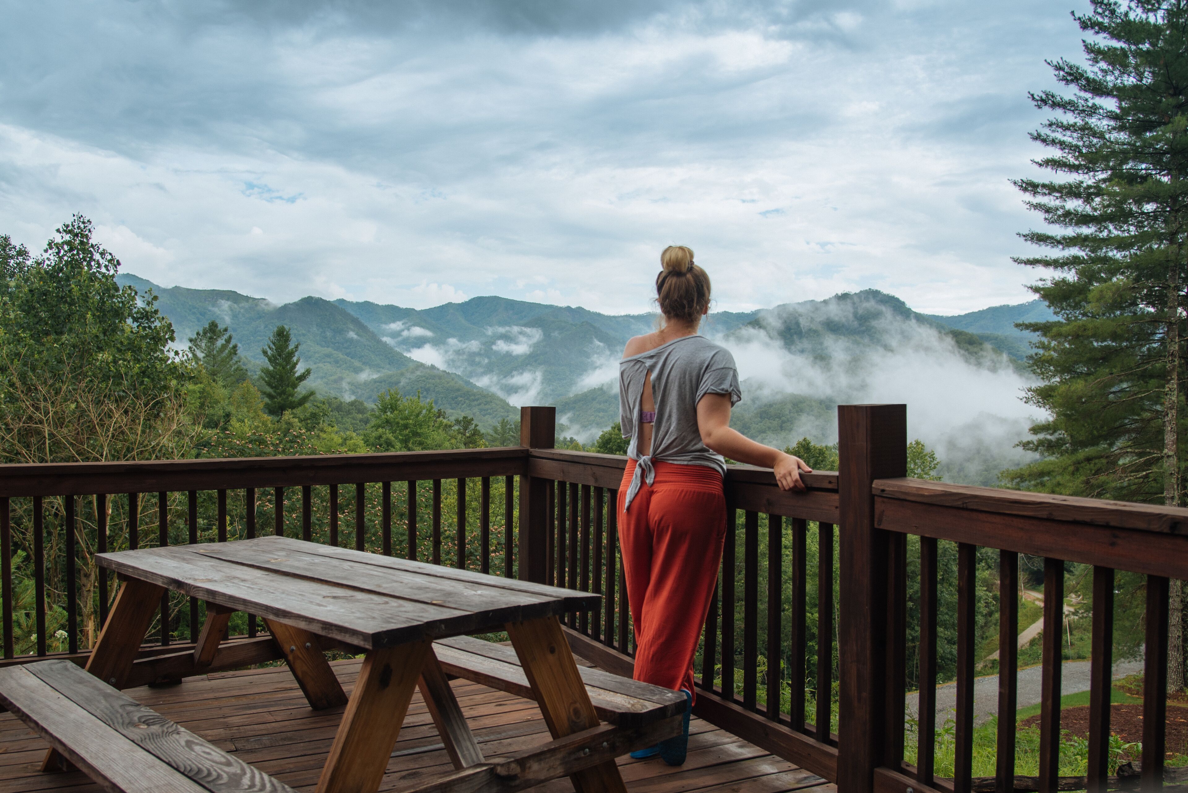 A wooden deck with a picnic table and a railing overlooking a mountainous landscape with trees and mist.