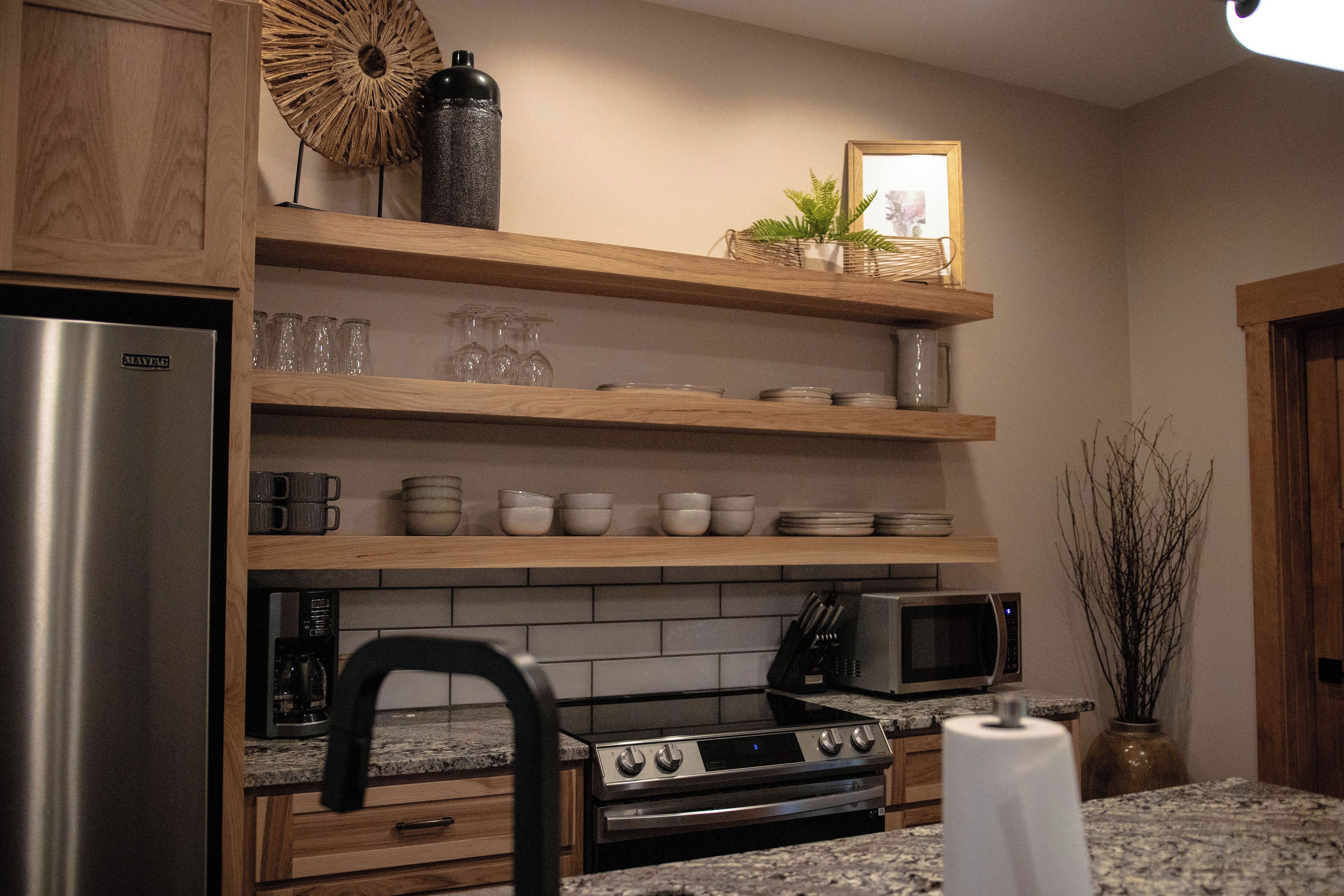 A kitchen with wooden shelves, a stainless steel refrigerator, a microwave, an oven, and a coffee maker.
