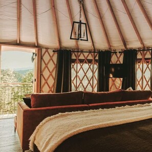 A cozy bed in a tent with a view of the outdoors.