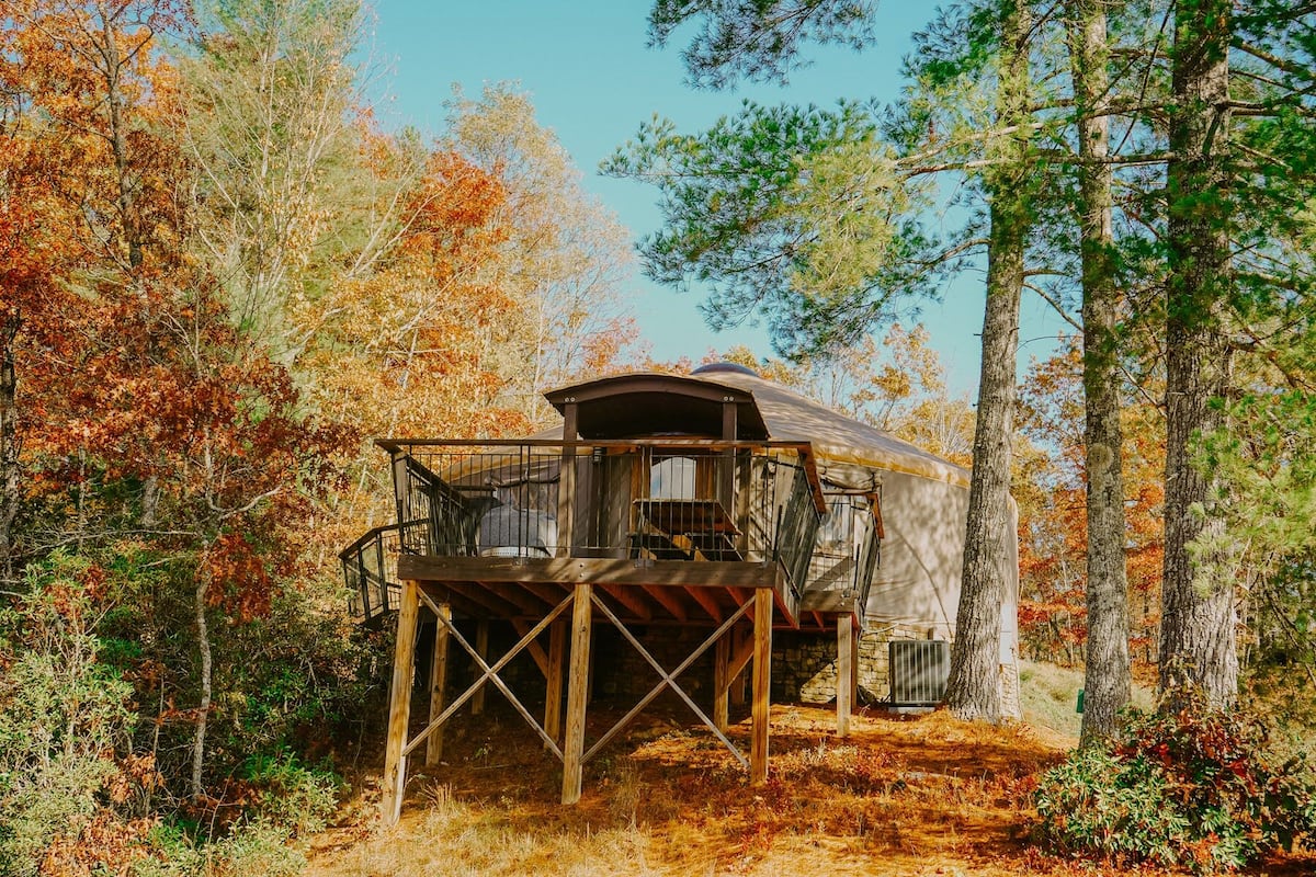 A rustic cabin with a balcony, surrounded by autumn foliage.