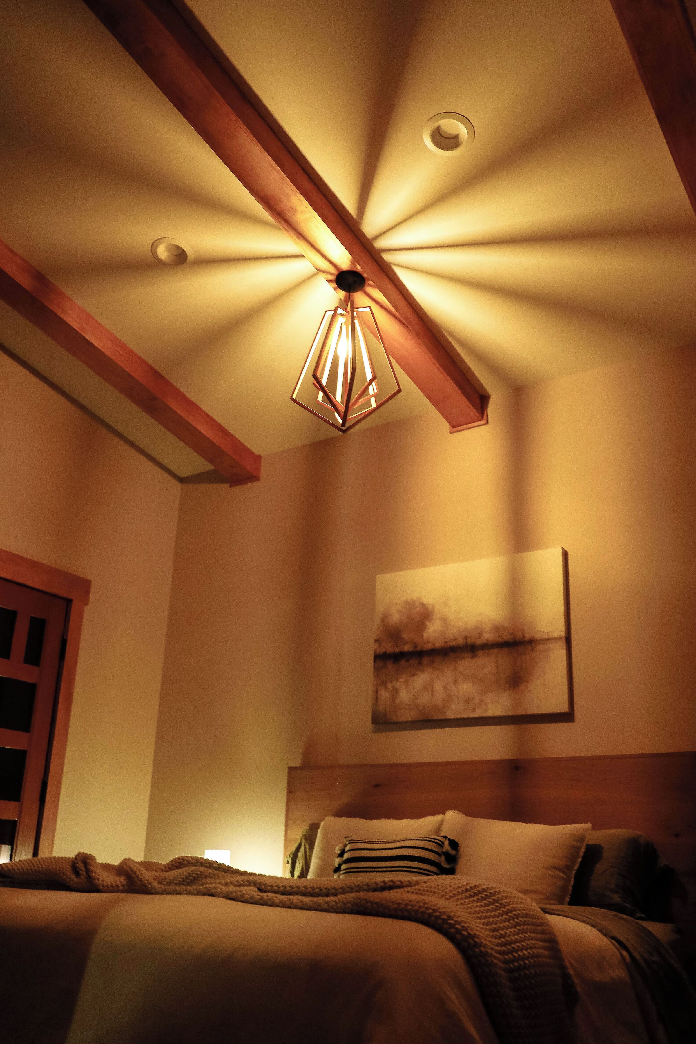 A bedroom with a bed, a wooden ceiling beam, recessed lighting, and a painting on the wall.