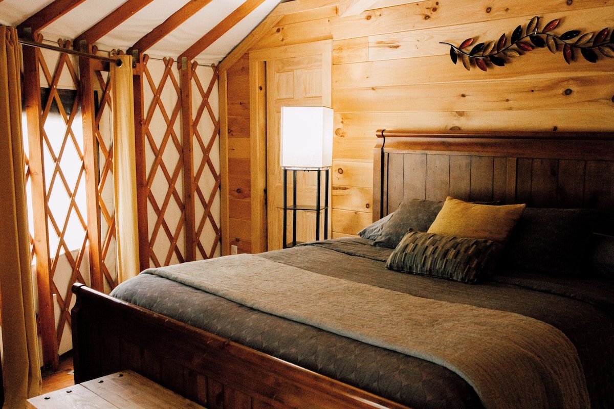 A wooden cabin bedroom with a bed, bench, and a window with curtains.