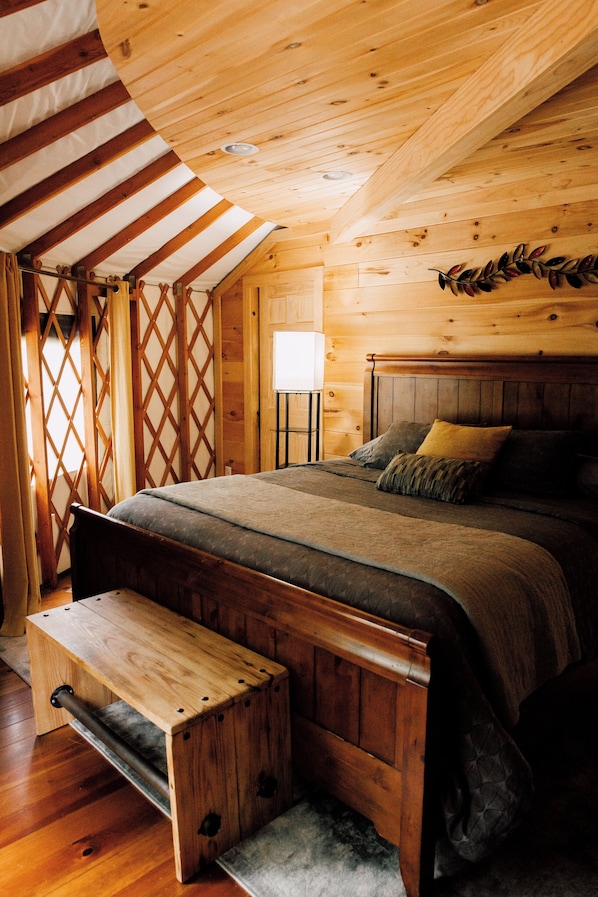 Une chambre dans une cabane en bois, avec un lit, un banc et une fenêtre avec des rideaux.