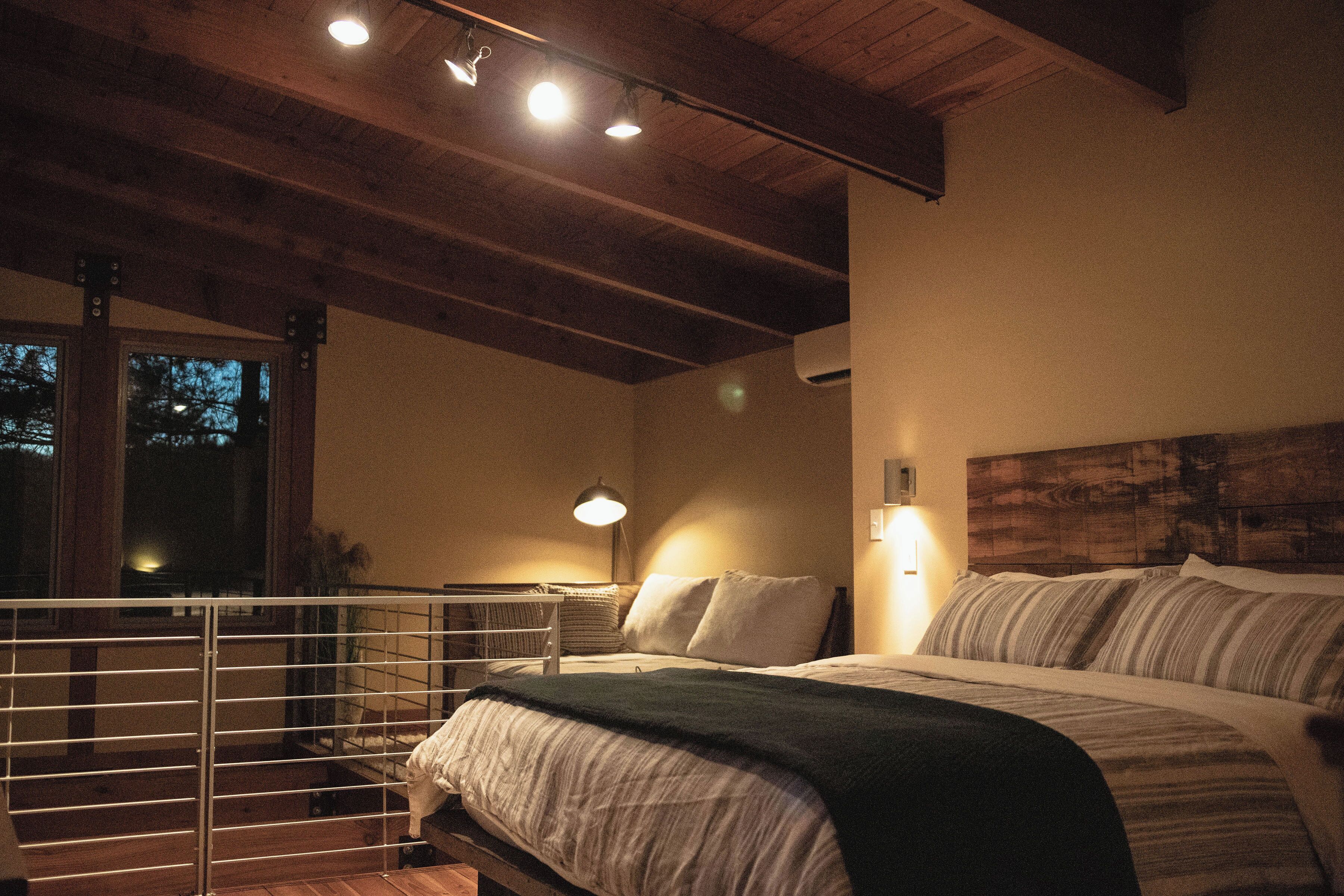 Un dormitorio con techo de madera, cama con ropa de cama a rayas, una mesita de noche y una lámpara.