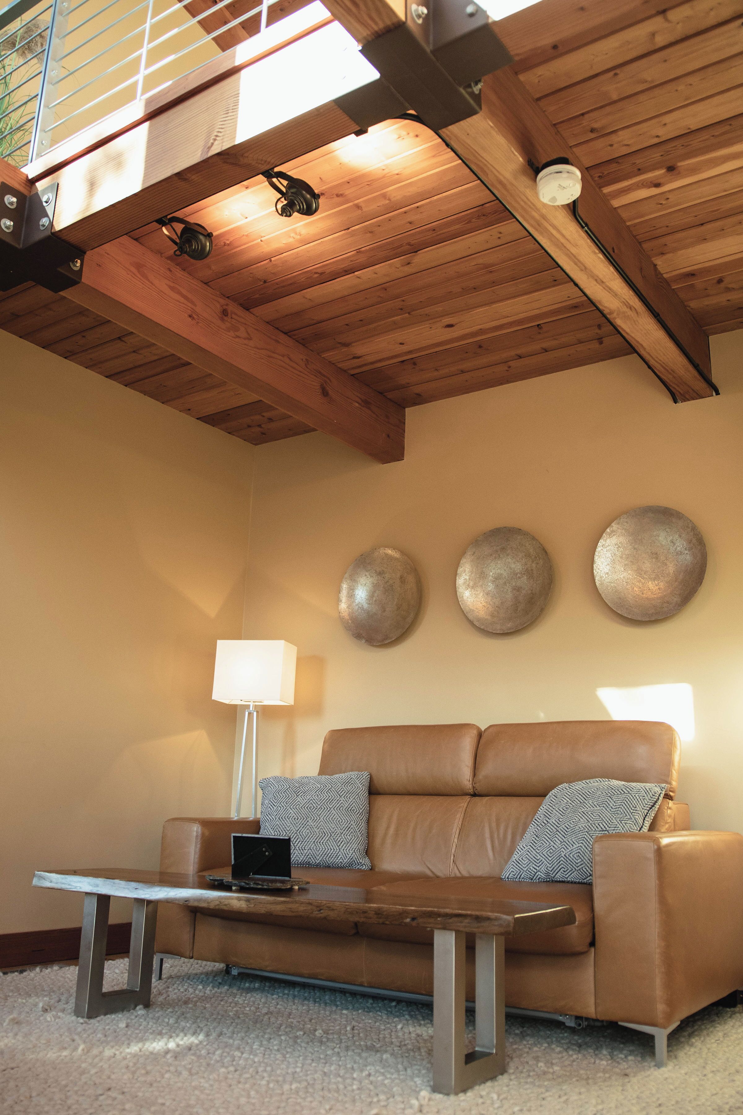 A cozy living room with a wooden ceiling, a leather sofa, a coffee table, and decorative wall plates.