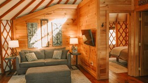 Interior acogedor de una cabaña de troncos con sofá, reposapiés y decoración mural.