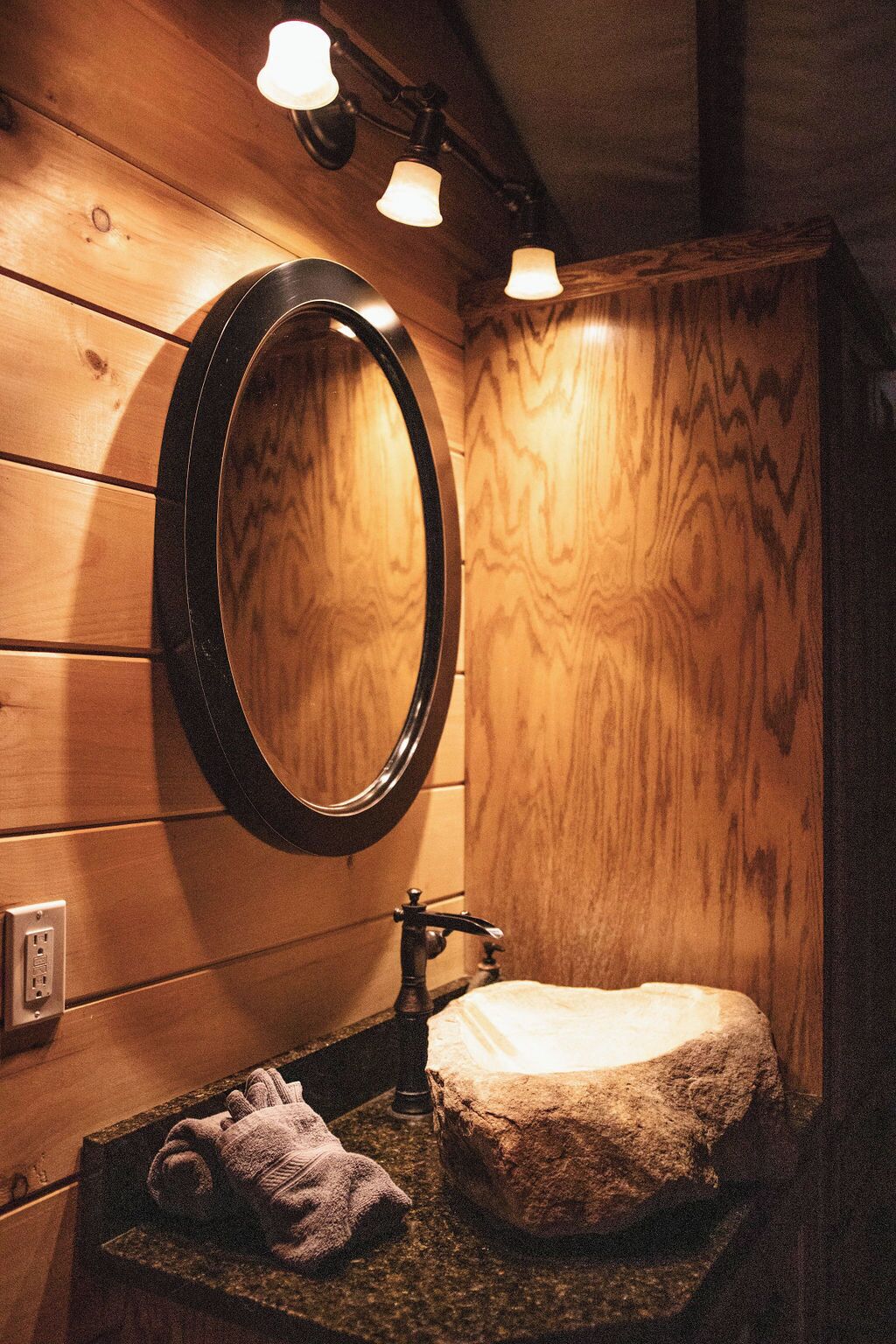 A wooden bathroom with a round mirror, a stone sink, and a towel on the counter.