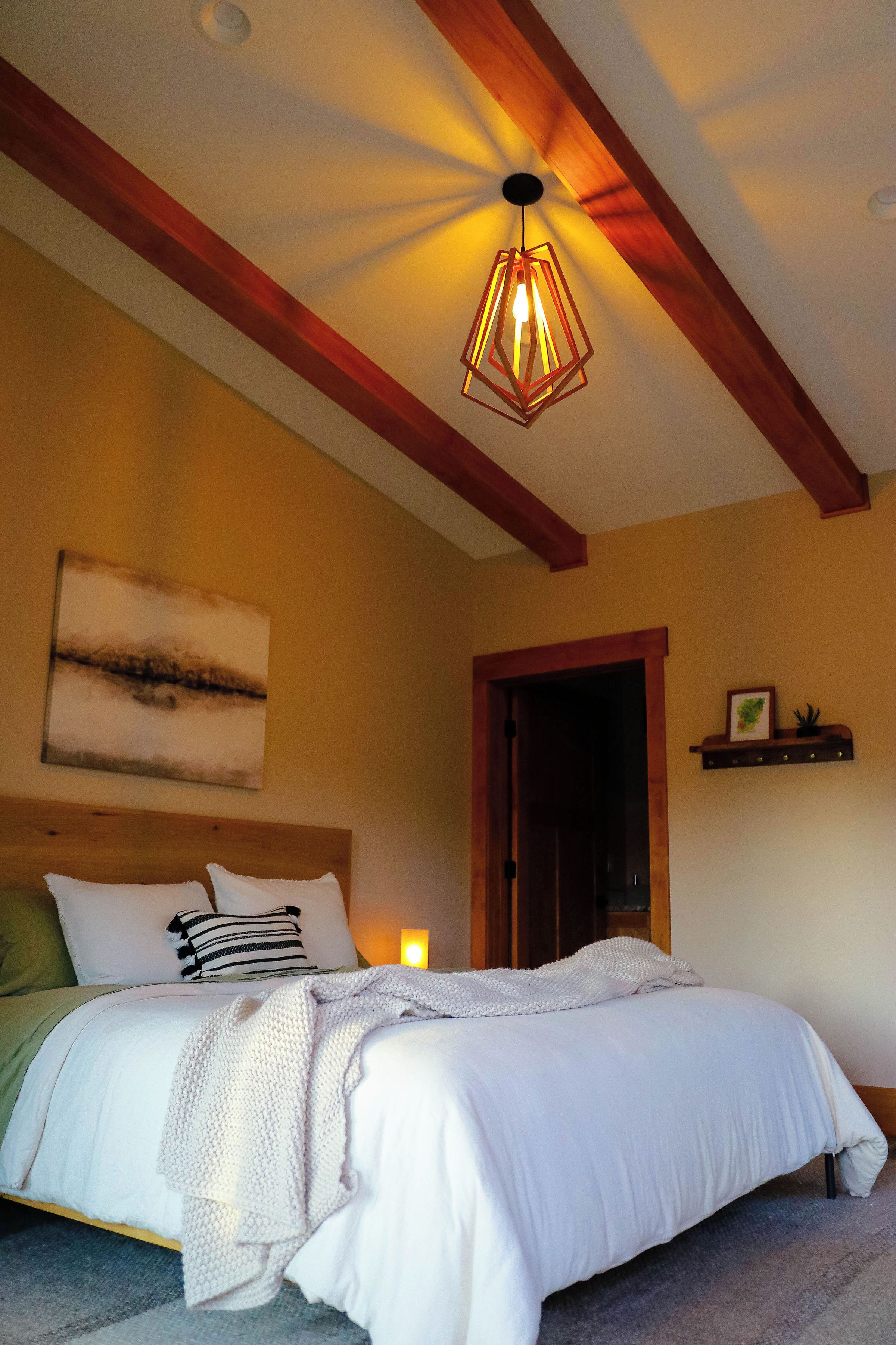 A bedroom with a bed, a hanging light fixture, a wooden headboard, a wall-mounted shelf, and a door.