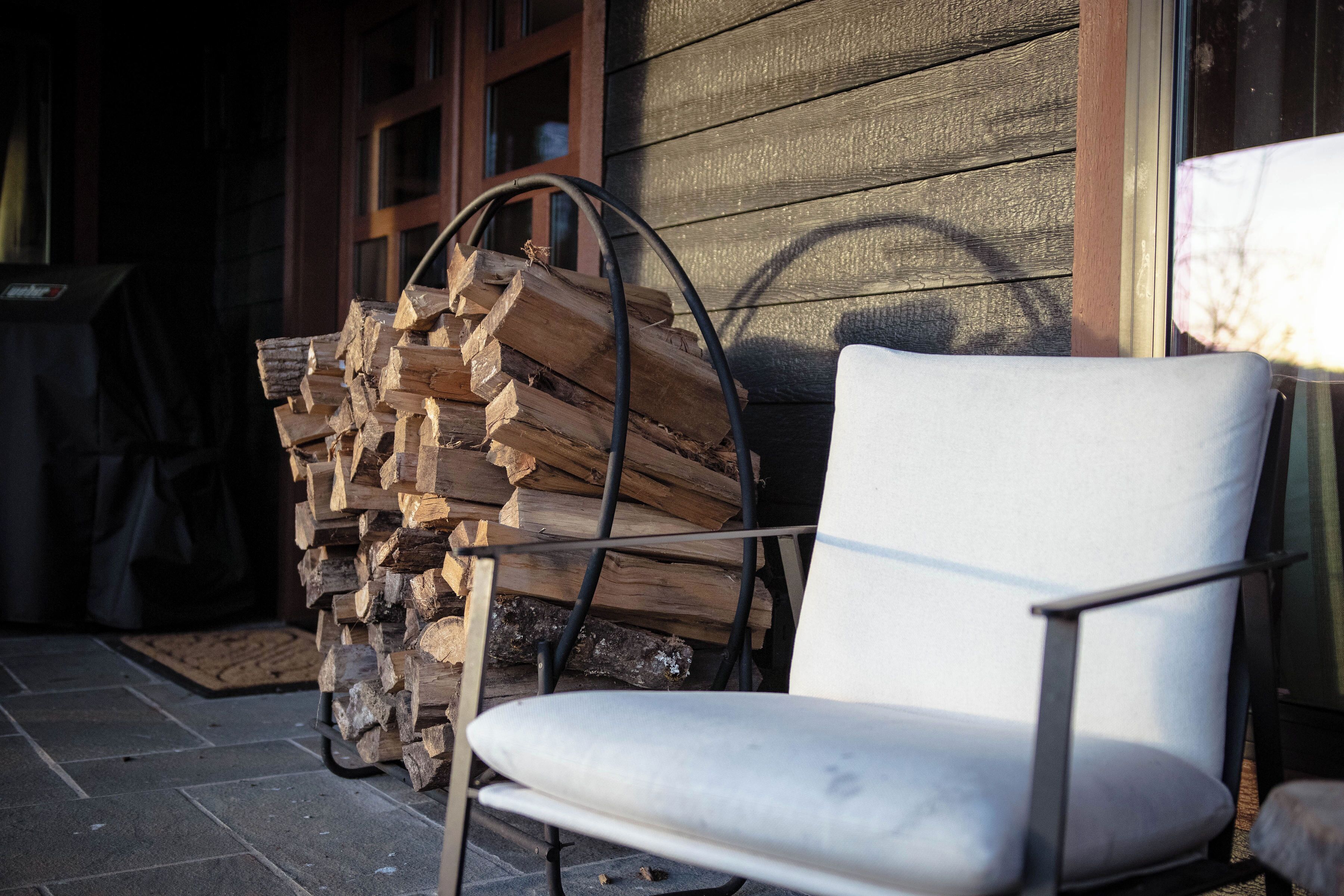 A chair outside a building with a stack of firewood nearby.