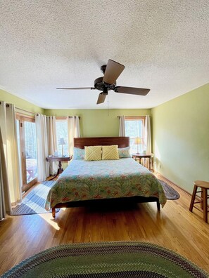 A bedroom with a bed, a ceiling fan, and a view of the outdoors through a window.