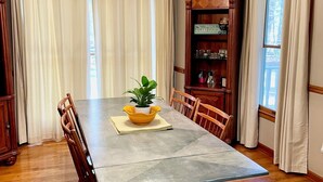 A dining room with a large table, wooden chairs, a chandelier, and a bookshelf.