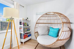 A room with a wicker chair, a standing lamp, a bookshelf, and a window with a view.