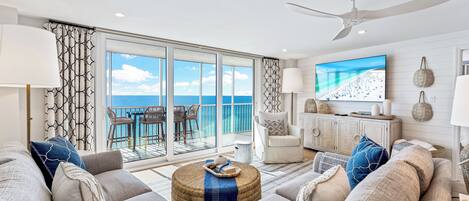 A spacious living room with a large sofa, a television, and a view of the ocean through a sliding glass door.