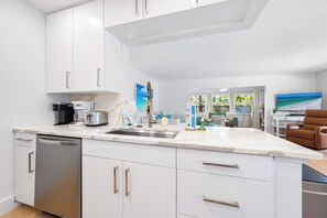 A modern kitchen with white cabinetry, a dishwasher, a coffee maker, and a large island with a sink.