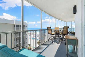 A balcony with a view of the beach, a table with chairs, and a trash bin.