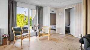 A spacious room with a wooden floor, two wicker chairs, a small round table with a vase, and a bed in the background. - 1 bedroom gorgeous home in Bogense (Bogense)