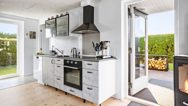 A modern kitchen with a built-in oven, a coffee machine, and a large window overlooking a garden. - 1 bedroom gorgeous home in Bogense (Bogense)