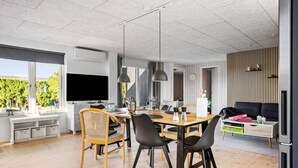 A modern living room with a dining area, large windows, and a flat-screen TV. - 1 bedroom gorgeous home in Bogense (Bogense)