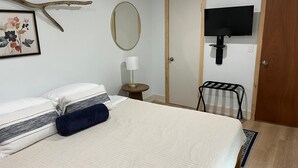 Ein ordentlich eingerichtetes Schlafzimmer mit Bett, Nachttischlampe, einem an der Wand montierten Fernseher und einer Tür.